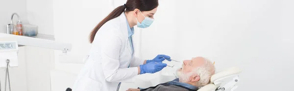 Dentista examinando dentes de homem idoso com sonda e espelho na clínica odontológica, banner — Fotografia de Stock