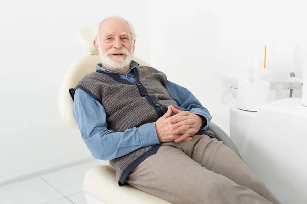 Uomo anziano seduto con le mani serrate in sedia dentale in clinica — Foto stock