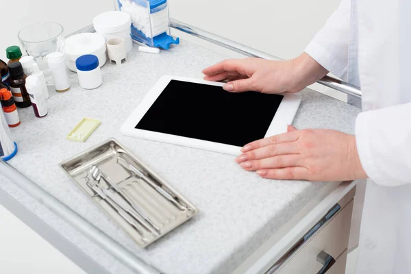 Vista recortada das mãos do dentista feminino usando tablet com tela em branco perto de ferramentas odontológicas de metal na bandeja — Fotografia de Stock