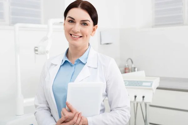 Smiling dentist standing with tablet in hands in dental clinic — Stock Photo