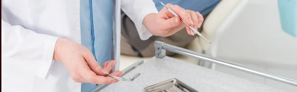 Vue recadrée des mains de dentiste tenant des outils en métal au-dessus d'un plateau en métal sur la table dans une clinique dentaire, bannière — Photo de stock