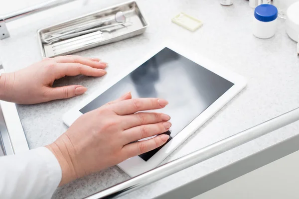 Частичный вид на урожай женских рук, печатающих на планшете с чистым экраном возле стоматологического оборудования на медицинском столе — стоковое фото