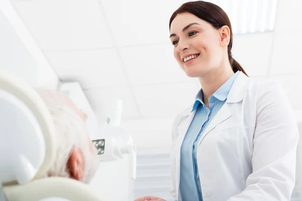 Dentista sorridente olhando para o paciente sênior na cadeira dentária — Fotografia de Stock