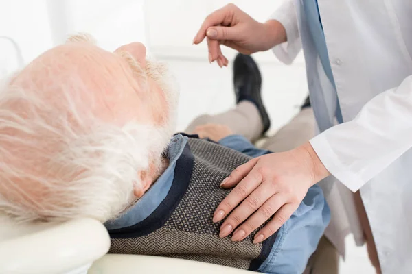 Paziente anziano sdraiato sulla sedia dentale con le mani del dentista toccare con attenzione la spalla in clinica — Foto stock