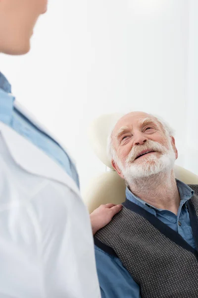 Paziente anziano sorridente sdraiato sulla sedia dentale con mano dentista sulla spalla — Foto stock