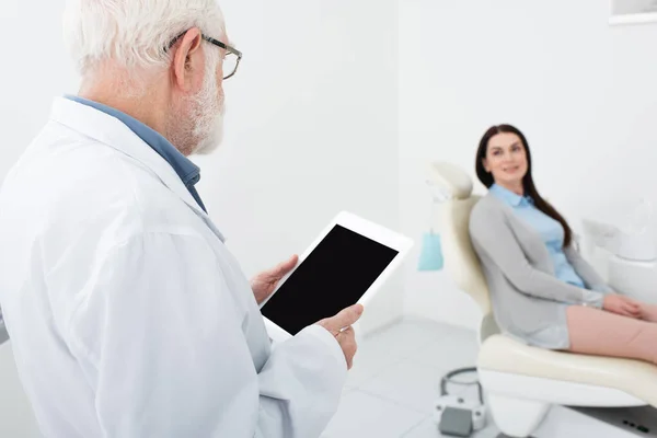 Dentista anziano in piedi con tablet davanti al paziente in clinica dentale — Foto stock