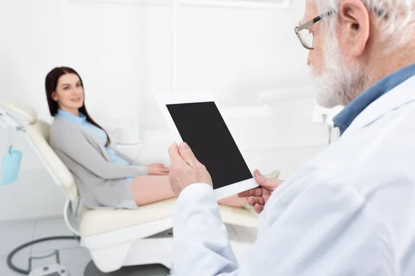 Dentista senior dando consulta al paciente borroso en silla dental y sosteniendo la tableta con pantalla en blanco en la clínica - foto de stock