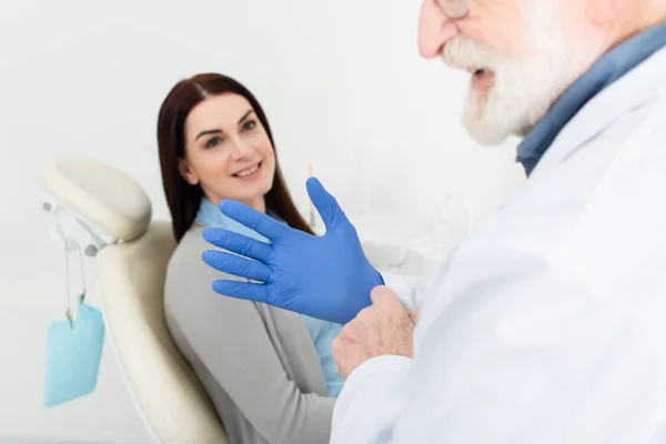 Dentista regolazione guanti in lattice prima dell'esame del paziente seduto sulla sedia dentale — Foto stock