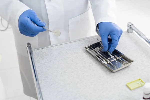 Ausgeschnittene Ansicht eines Arztes in Latexhandschuhen, der in der Klinik zahnärztliche Metallgeräte aus dem Tablett holt — Stock Photo