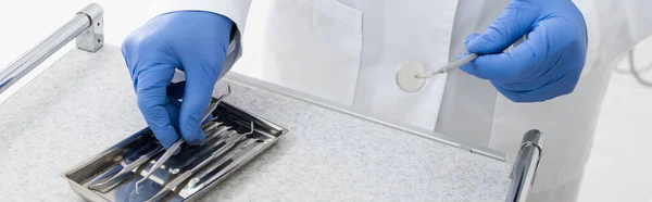 Cropped view of dentist in latex gloves taking medical equipment from tray on medical table, banner — Stock Photo