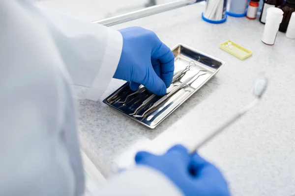 Обрізаний вид на стоматолога в латексних рукавичках, що приймають медичне обладнання з лотка на медичний стіл — стокове фото