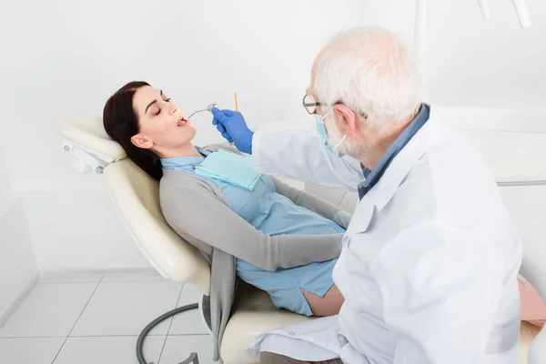 Старший стоматолог делает лечение зубов пациента в стоматологическом кресле — стоковое фото