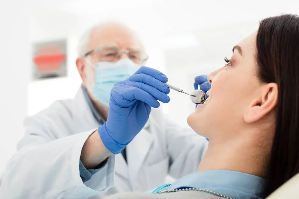 Старший стоматолог осматривает зубы взрослой женщины с зондом и зеркалом в стоматологической клинике — стоковое фото