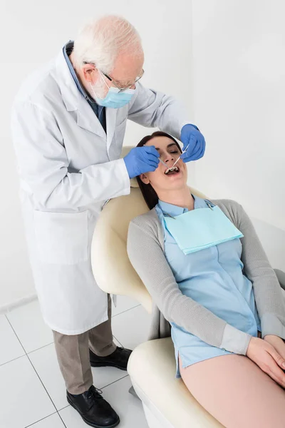 Dentista sênior fazendo exame de mulher na cadeira dentária na clínica — Fotografia de Stock