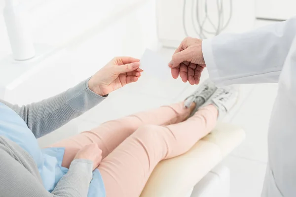 Vista parcial de las manos del paciente y del dentista masculino sosteniendo la tarjeta vacía en la clínica dental - foto de stock