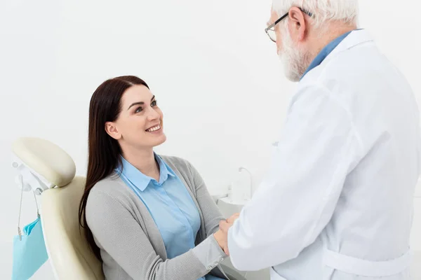Patient souriant dans la chaise dentaire tenant la main du médecin principal à la clinique — Photo de stock