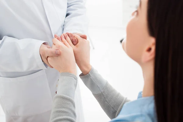 Brunette woman sitting and holding hands of doctor in clinic — Stock Photo