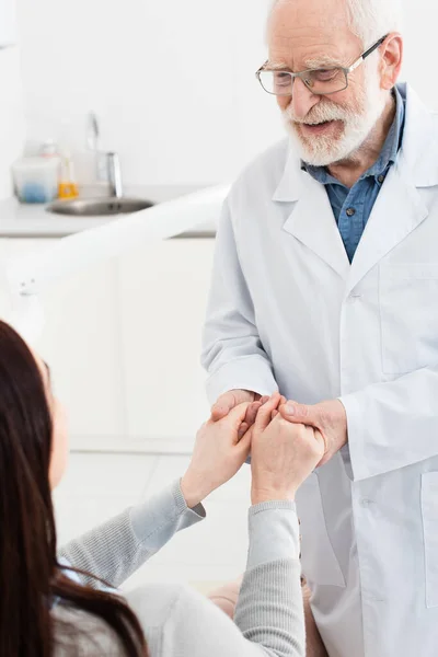 Dentiste sénior joyeux tenant la main du patient dans une clinique dentaire — Photo de stock