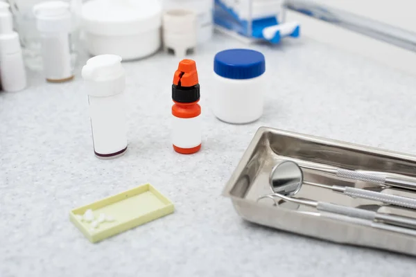 Vue grand angle des médicaments et outils dentaires dans un plateau métallique et sur une table médicale — Photo de stock