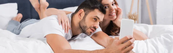 Mujer borrosa abrazando novio durante selfie en el dormitorio, pancarta - foto de stock