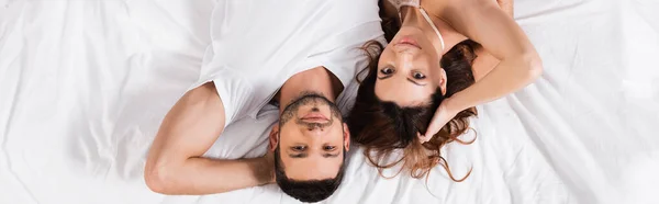Vue du dessus du jeune couple regardant la caméra sur le lit, bannière — Photo de stock