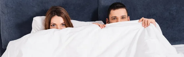 Pareja joven cubriendo caras con manta en la cama, pancarta - foto de stock