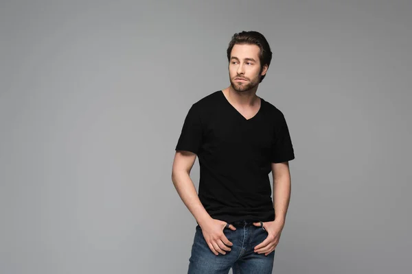 Junger bärtiger Mann in schwarzem T-Shirt und Jeans schaut weg und posiert isoliert auf grauem Grund — Stockfoto
