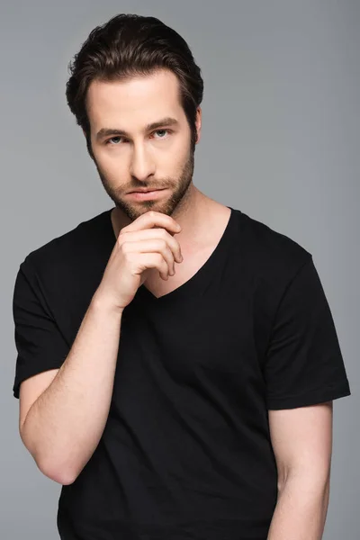 Pensive man in black t-shirt looking at camera while posing isolated on gray — Stock Photo