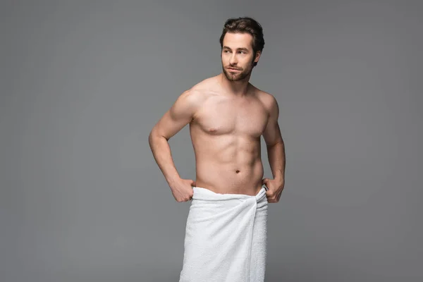 Hombre sin camisa ajustando la toalla y de pie aislado en gris - foto de stock