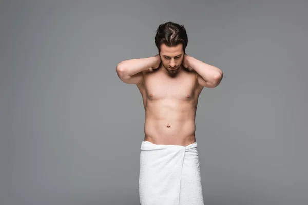Мускулистый человек завернутый в полотенце стоя и глядя вниз изолированы на серый — стоковое фото