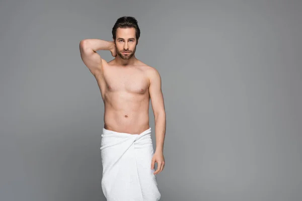 Uomo muscoloso avvolto in asciugamano bianco posa isolato su grigio — Foto stock