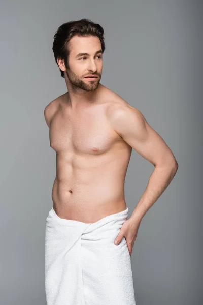 Молодой мускулистый мужчина, завернутый в белое полотенце, смотрит в сторону, изолированный на сером — стоковое фото