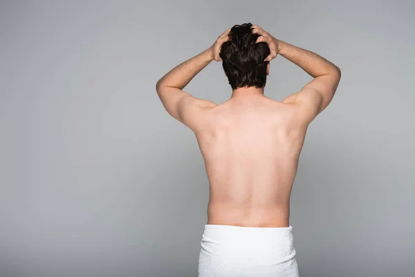 Vista posterior del hombre sin camisa envuelto en toalla ajustando el cabello aislado en gris - foto de stock