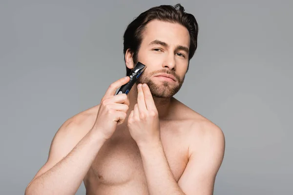 Uomo senza maglietta con barba utilizzando rasoio elettrico isolato su grigio — Foto stock