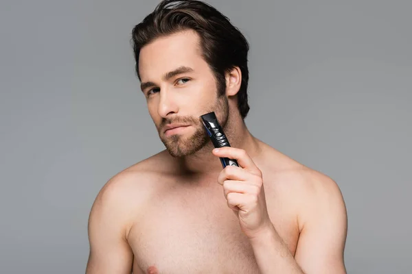 Без рубашки мужчина обрезать бороду с электрическим триммером изолированы на сером — стоковое фото