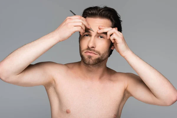 Бородатый и без рубашки мужчина выщипывая брови изолированы на сером — стоковое фото