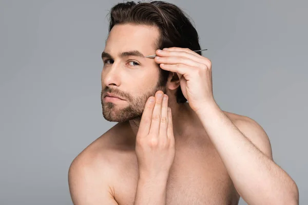 Bearded and shirtless man tweezing eyebrow isolated on grey — Stock Photo