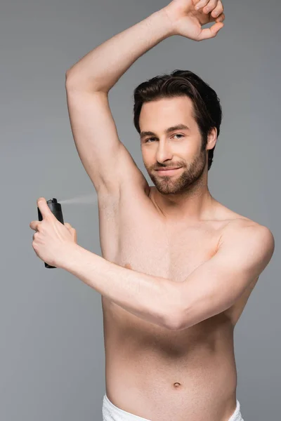 Smiling and shirtless man with raised hand spraying antiperspirant isolated on grey — Stock Photo