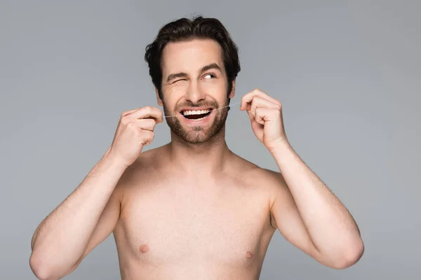 Shirtless man winking eye while flossing teeth isolated on grey — Stock Photo