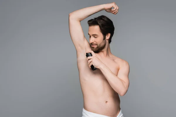 Hombre barbudo y sin camisa con la mano levantada usando antitranspirante aislado en gris - foto de stock