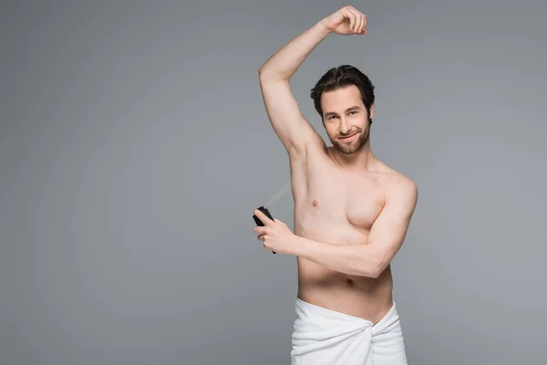 Homem feliz e sem camisa com a mão levantada usando antitranspirante isolado em cinza — Stock Photo