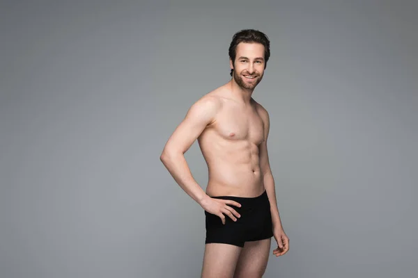 Happy shirtless man in black underwear posing with hand on hip isolated on grey — Stock Photo