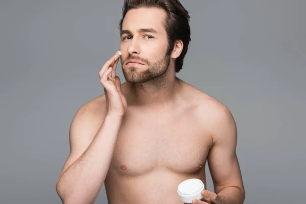 Мужчина без рубашки наносит увлажняющий крем для лица, изолированный на сером — стоковое фото