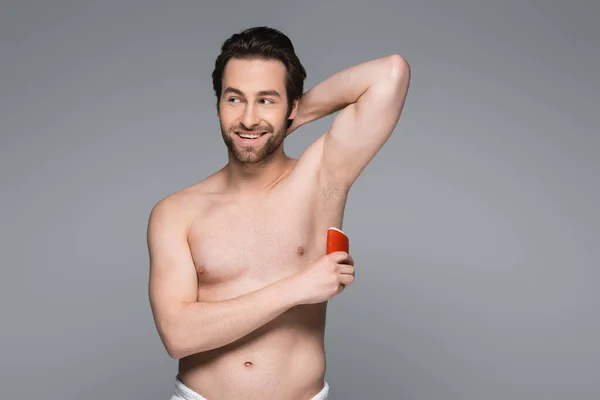 Веселый мужчина без рубашки, нанося твердую палку дезодорант изолирован на серый — стоковое фото