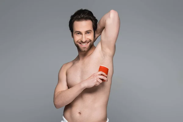 Homem sem camisa alegre aplicando desodorizante de pau sólido isolado em cinza — Fotografia de Stock
