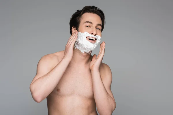 Hombre feliz y sin camisa con espuma de afeitar blanca de la cara aislada en gris - foto de stock