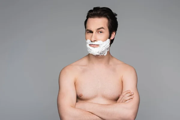 Hombre sin camisa con espuma de afeitar de cara posando con brazos cruzados aislados en gris - foto de stock