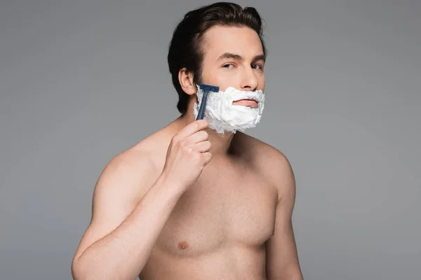 Hemdloser Mann mit Schaum im Gesicht rasiert mit Sicherheitsrasierer isoliert auf grau — Stockfoto