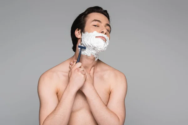 Мужчина без рубашки с белой пеной на лице бритья с безопасной бритвой изолированы на сером — стоковое фото