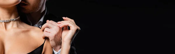 Vista recortada del hombre en blazer negro y camisa blanca suavemente desvestirse mujer aislado en negro, bandera - foto de stock